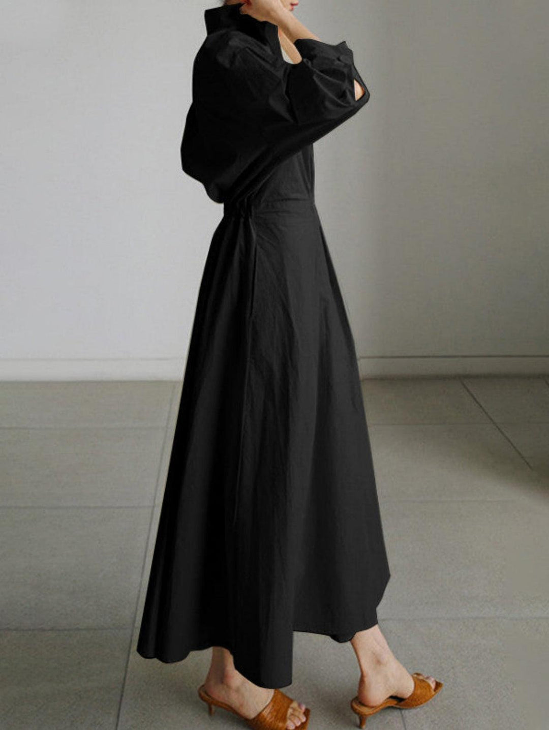 Side view of black midi dress with button lapel, worn with brown sandals indoors.