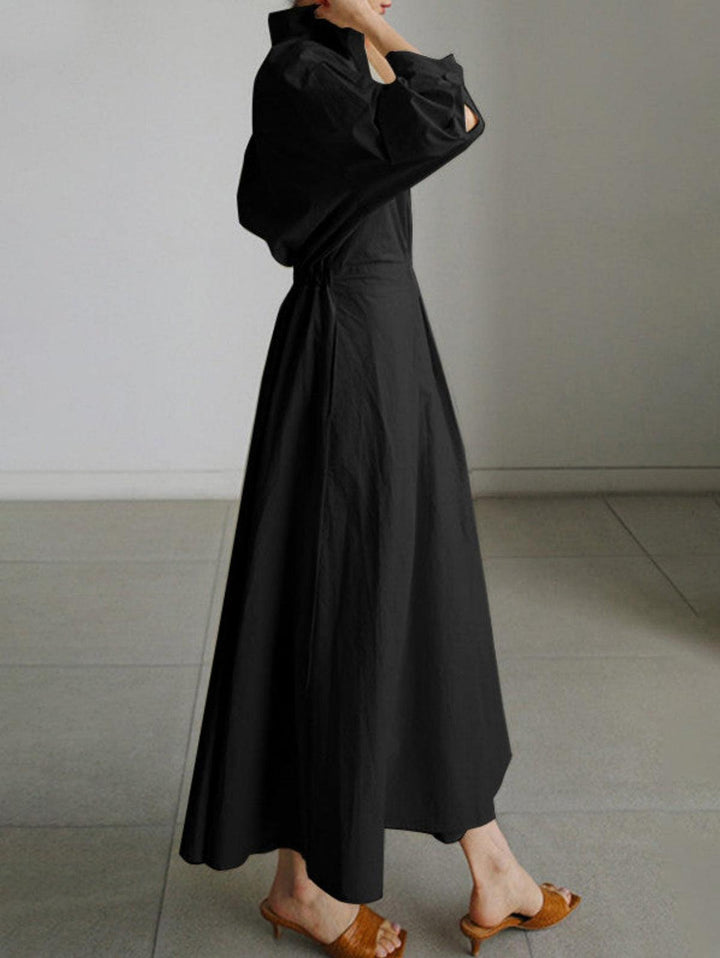 Side view of black midi dress with button lapel, worn with brown sandals indoors.