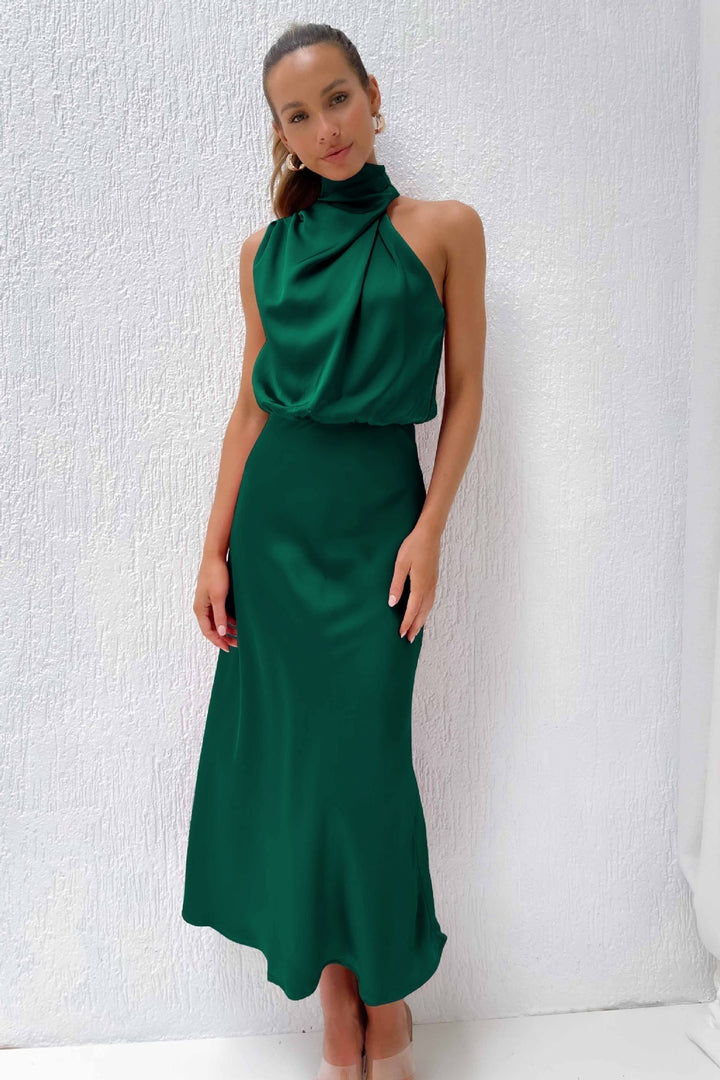 Teal sleeveless halter dress with an elegant cut against a textured white wall.