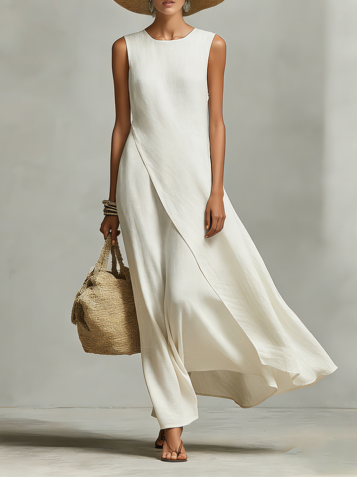 Woman in an ivory loose-fit maxi dress holding a woven bag, wearing a wide-brimmed hat, standing in a studio setting.