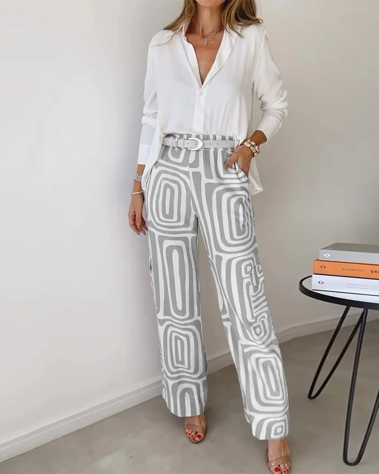 Elegant two-piece set with a white blouse and gray geometric-patterned pants. Styled in a minimalist indoor setting.