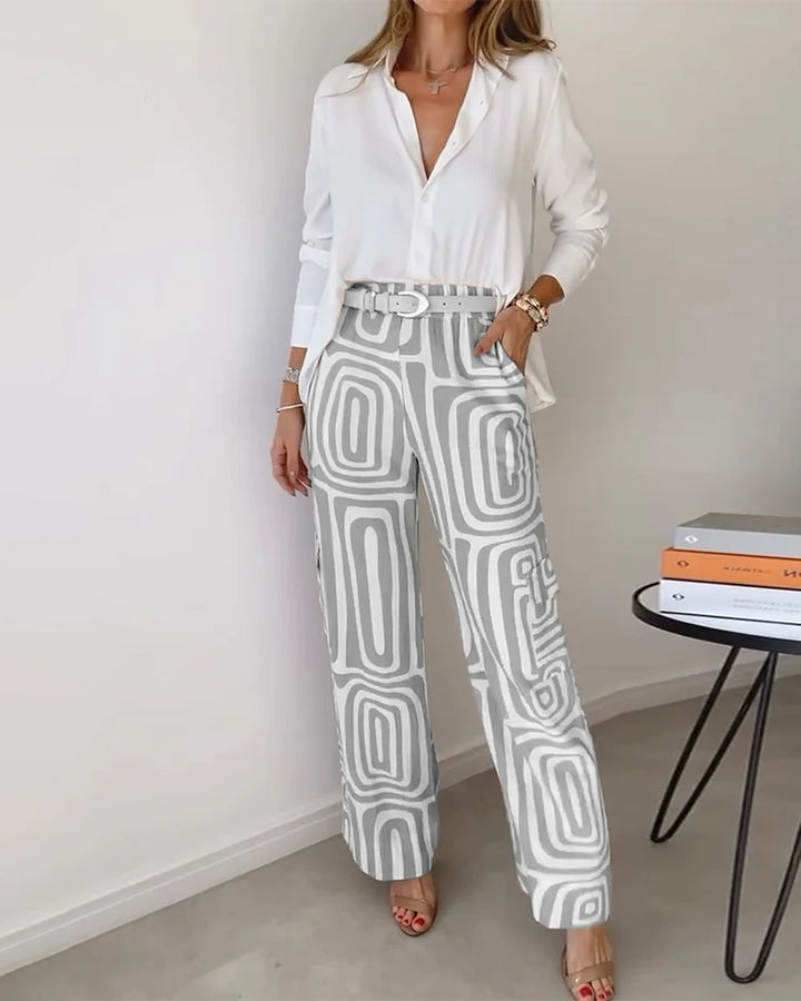 Elegant two-piece set with a white blouse and gray geometric-patterned pants. Styled in a minimalist indoor setting.