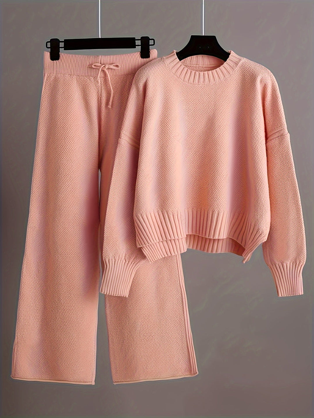 Light pink knit loungewear set with a soft sweater and loose pants on hangers, gray background.