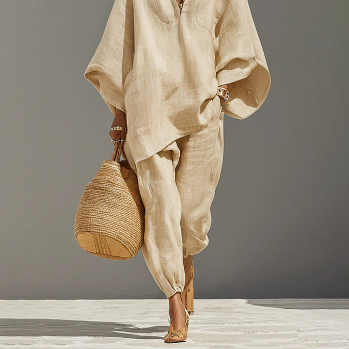 Close-up of beige batwing sleeve V-neck lounge set with woven bag, studio background.