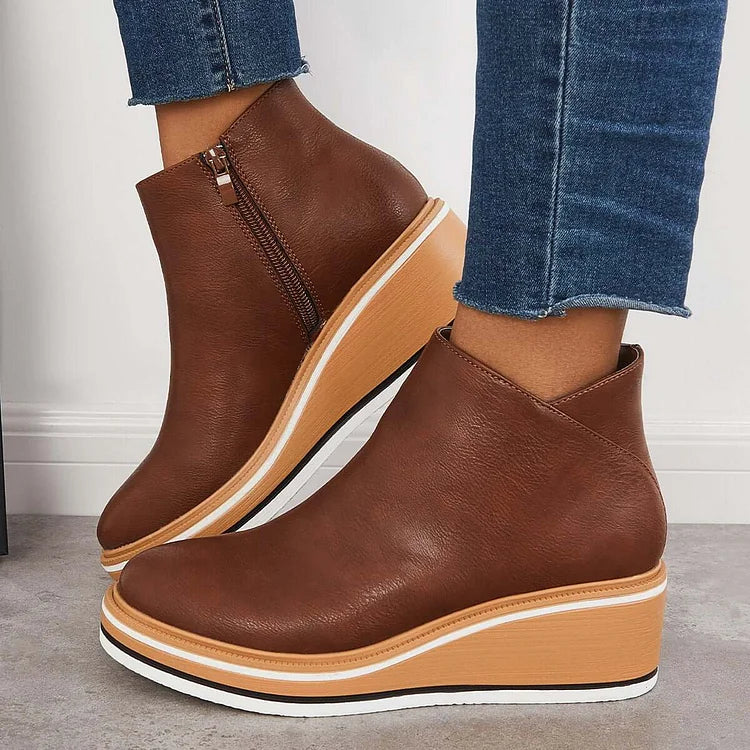 Brown luxe boots with wedge sole and zipper, paired with frayed jeans, on a gray floor and white wall.