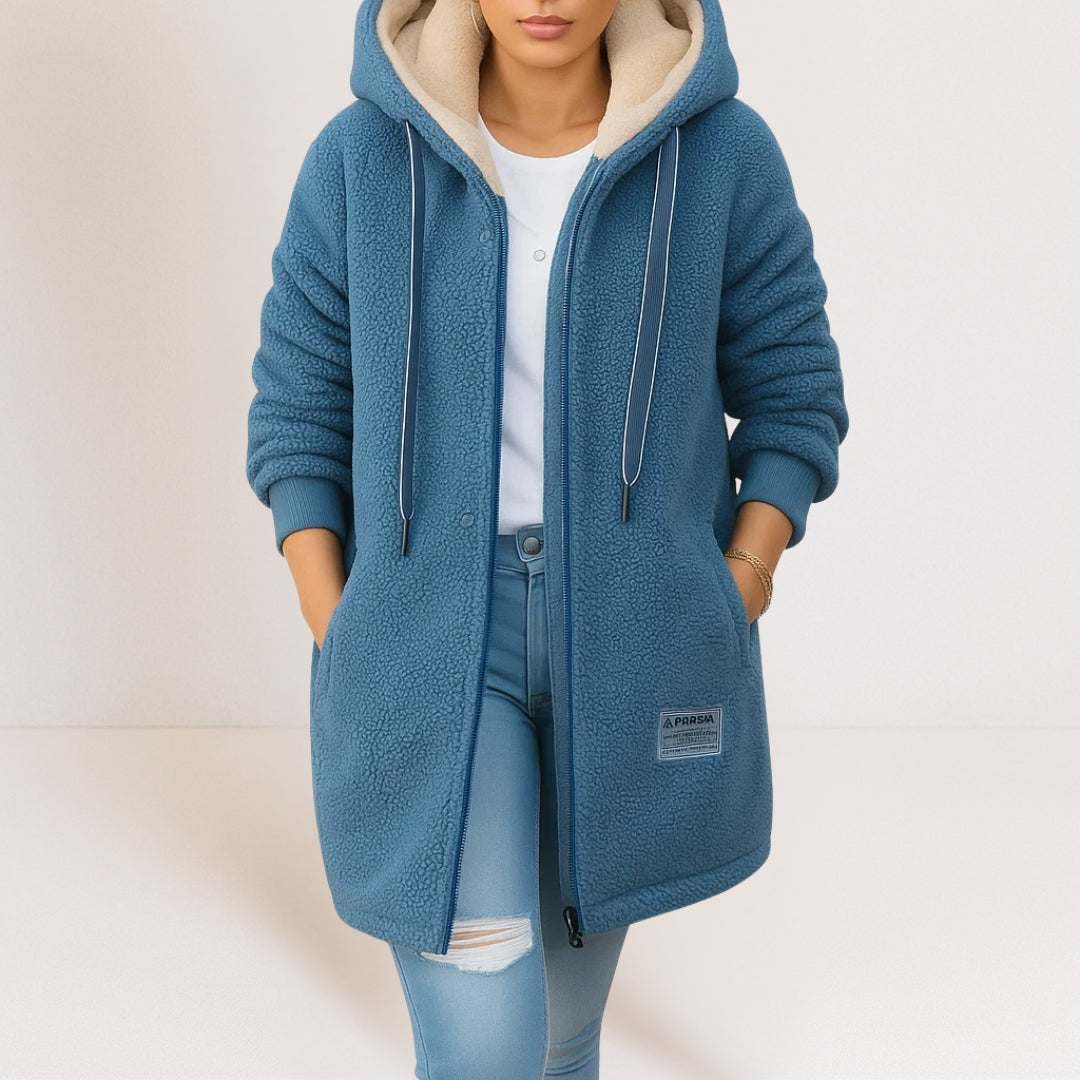 Woman wearing a blue soft jacket with a hood, drawstrings, and pockets, paired with light blue jeans in a studio setting.