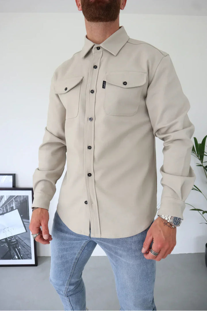 Light beige buttoned overshirt over white t-shirt and jeans, standing indoors.