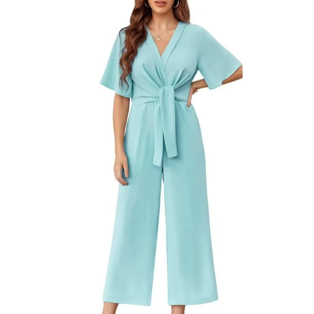 Light blue elegant jumpsuit with short sleeves and a tie waist on a woman, studio background.