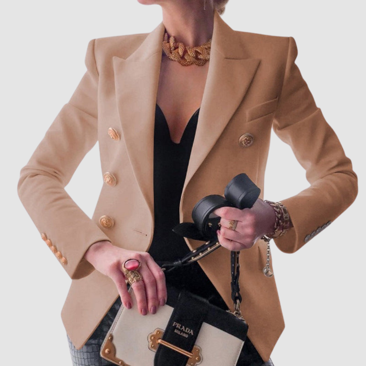 Chic beige blazer with gold buttons, worn over a black top. Gold accessories and beige handbag complete the look in a studio setting.