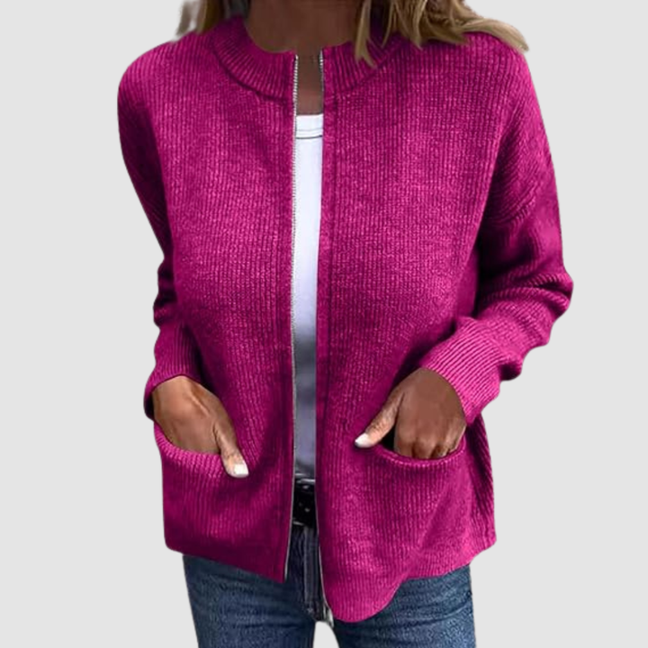Pink cozy cardigan worn over a white t-shirt with hands in pockets. Neutral background.
