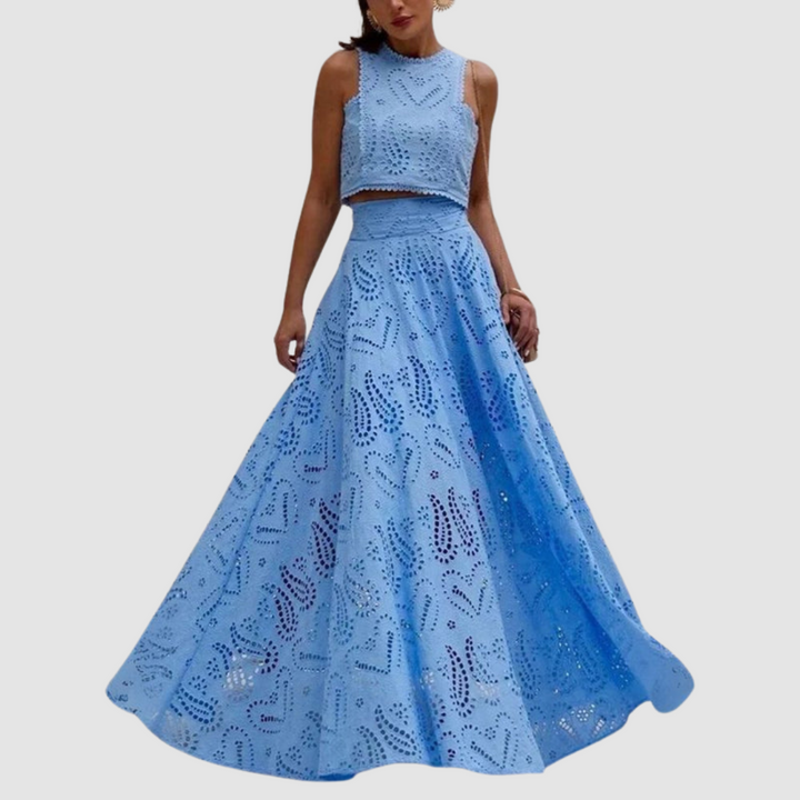 Woman wearing a blue two-piece set with detailed cutout design, flowing skirt, standing in a relaxed pose on a white background.