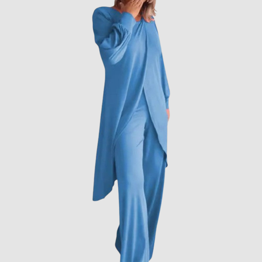 Model wearing a blue long-sleeve 2-piece set in a studio, hand covering face, white background.