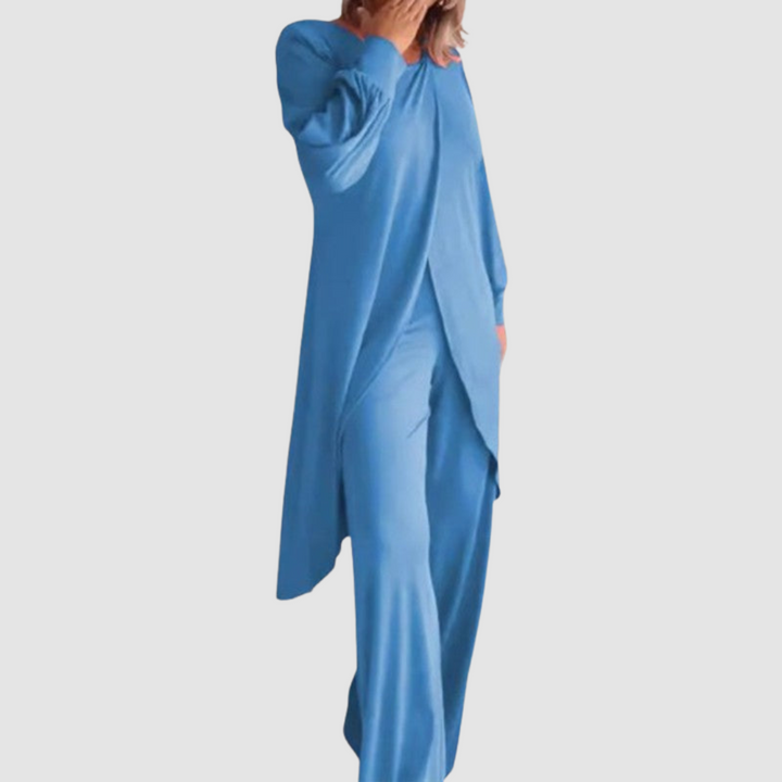 Model wearing a blue long-sleeve 2-piece set in a studio, hand covering face, white background.
