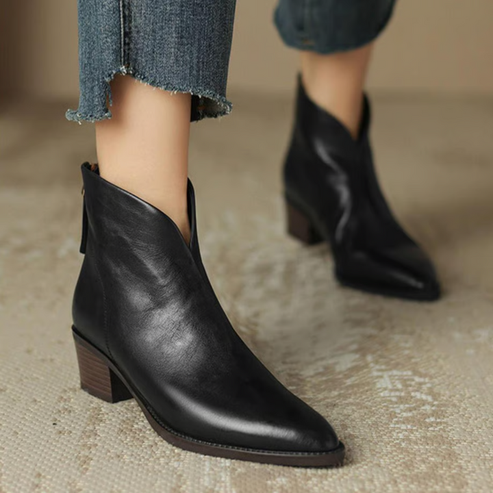 Black ankle boots with pointed toes, styled with frayed blue jeans on a neutral textured floor.
