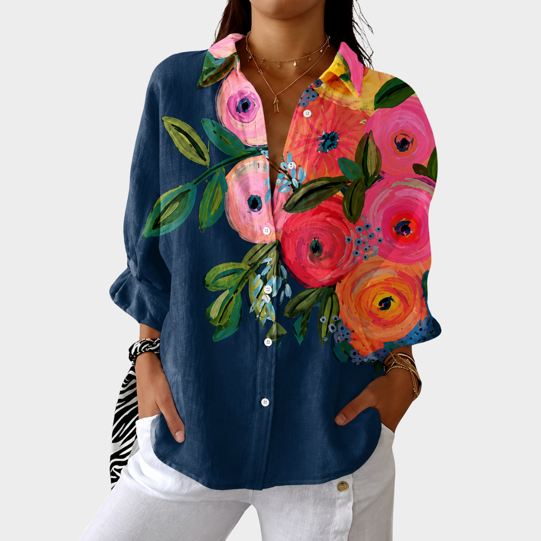 Woman wearing a navy blouse with vibrant floral prints in pink, orange, and green. Styled with white pants in a studio setting.