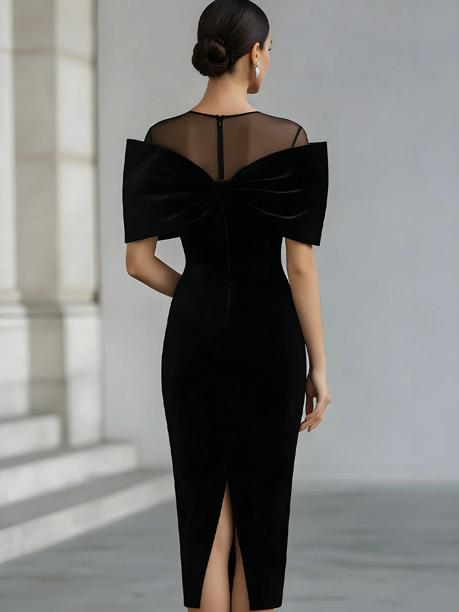 Back view of black midi dress featuring sheer panel and bow detail, modeled in a neutral studio setting.