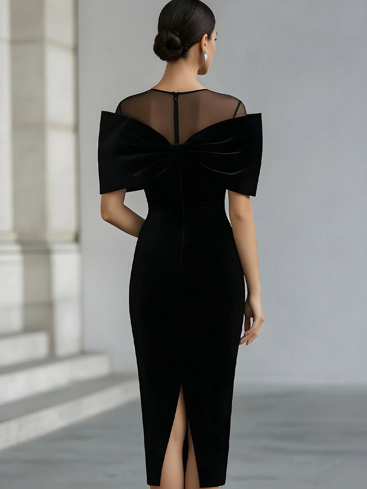 Back view of black midi dress featuring sheer panel and bow detail, modeled in a neutral studio setting.