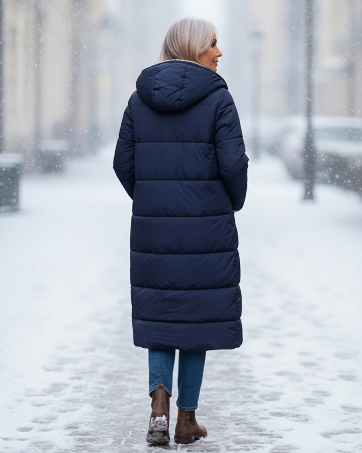 Back view of woman in blue coat, walking on a snowy city street.