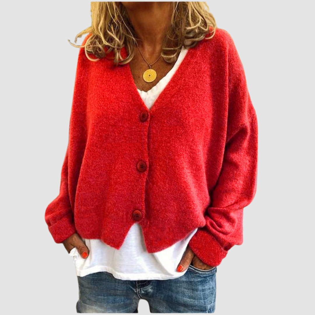 Woman wearing a red knit cardigan over a white shirt and blue jeans, set against a plain gray background.