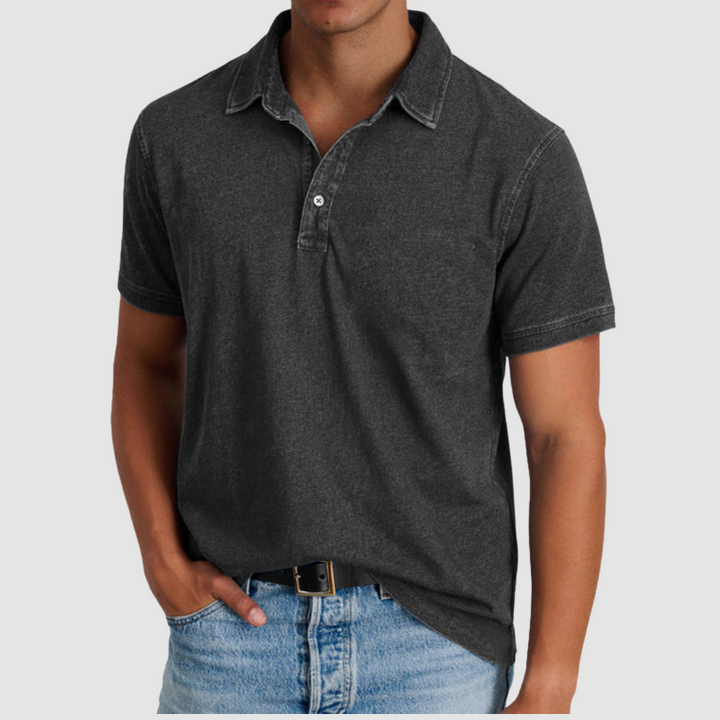Man wearing a dark grey classic collared polo with short sleeves, button placket, light jeans, studio backdrop.