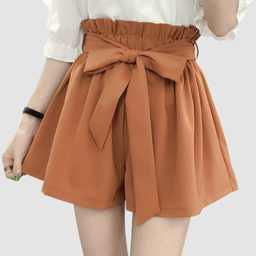 Orange paperbag waist shorts with a bow, paired with a white top in a studio background.