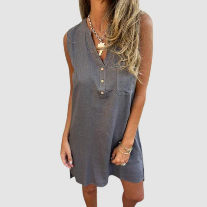Woman in a dark sleeveless dress with button details, accessorized with bracelets in a studio setting.