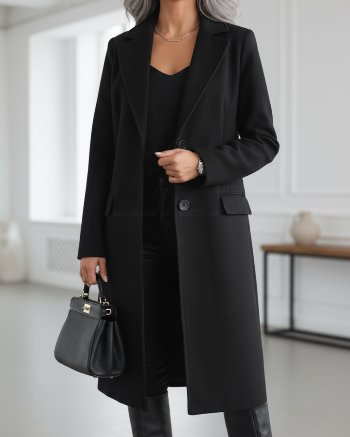 Black long coat with button front, worn over black attire, paired with a handbag in a stylish, modern interior.