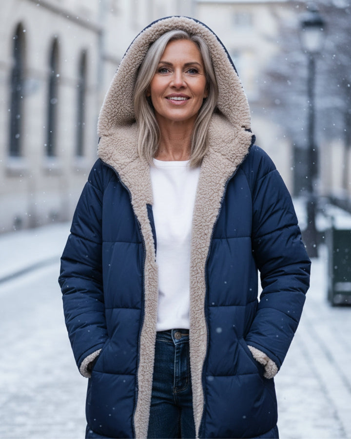 Woman in blue hooded coat, smiling in a snow-covered urban street.