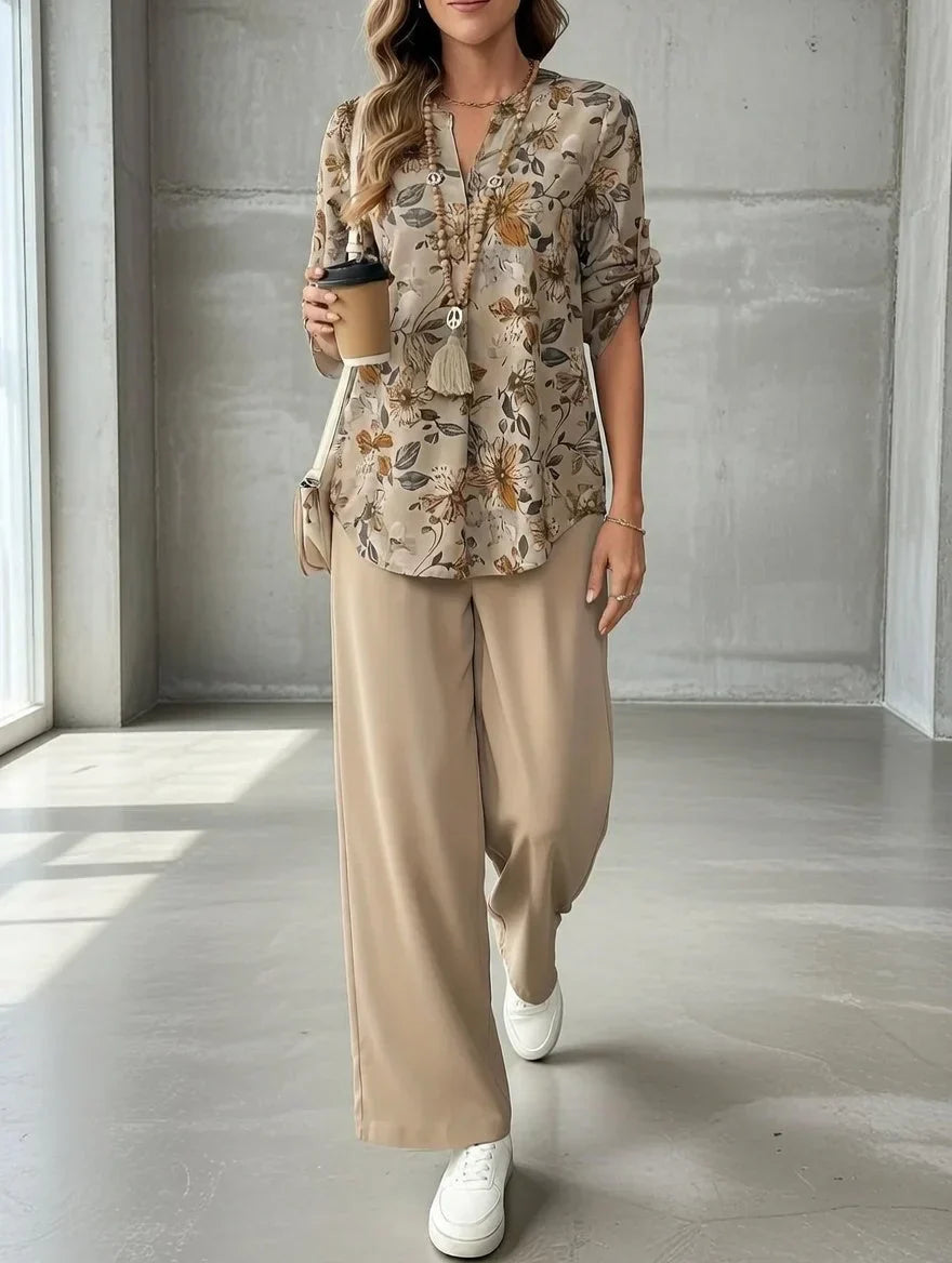 Individual holding a coffee cup, wearing a floral top and beige trousers in a bright, concrete-floored room.