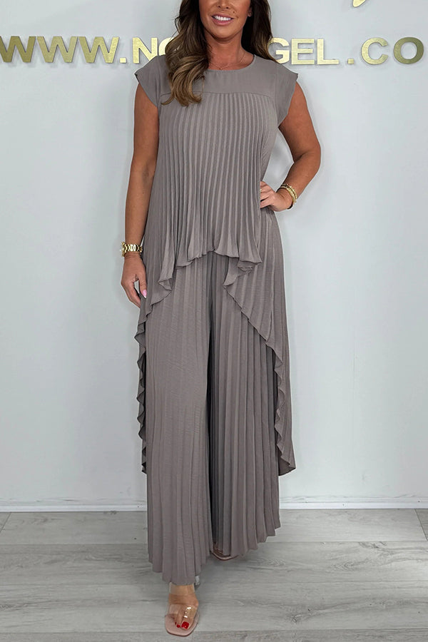 Woman wearing a taupe pleated midi top and wide-leg pants set, standing in a studio with a neutral wall and floor.