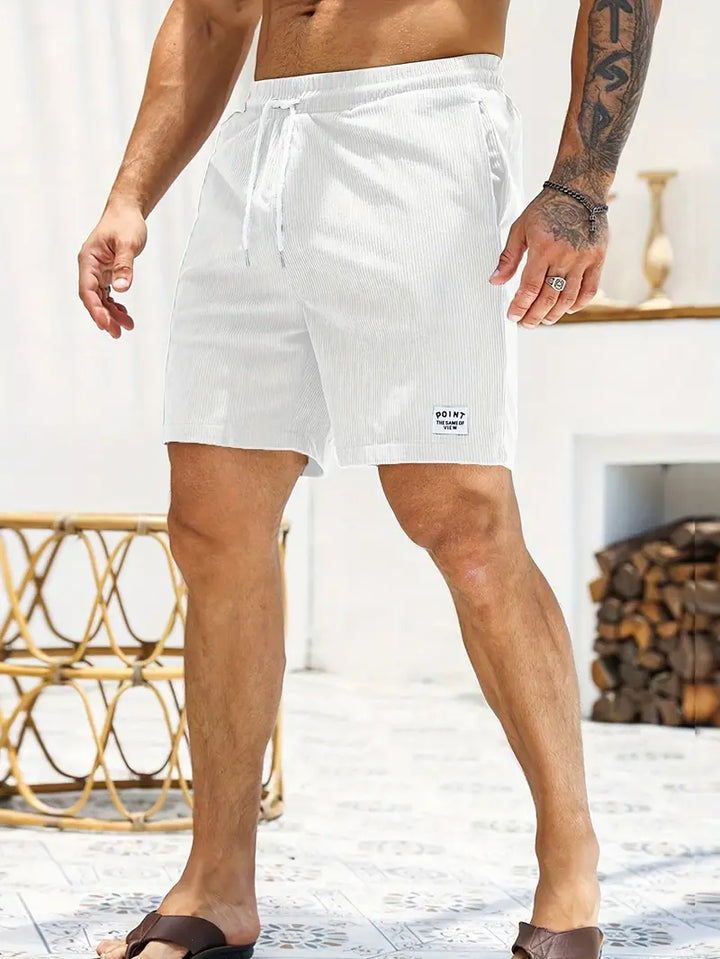Model standing in white swimming trunks with drawstring, indoor setting with sleek decor.