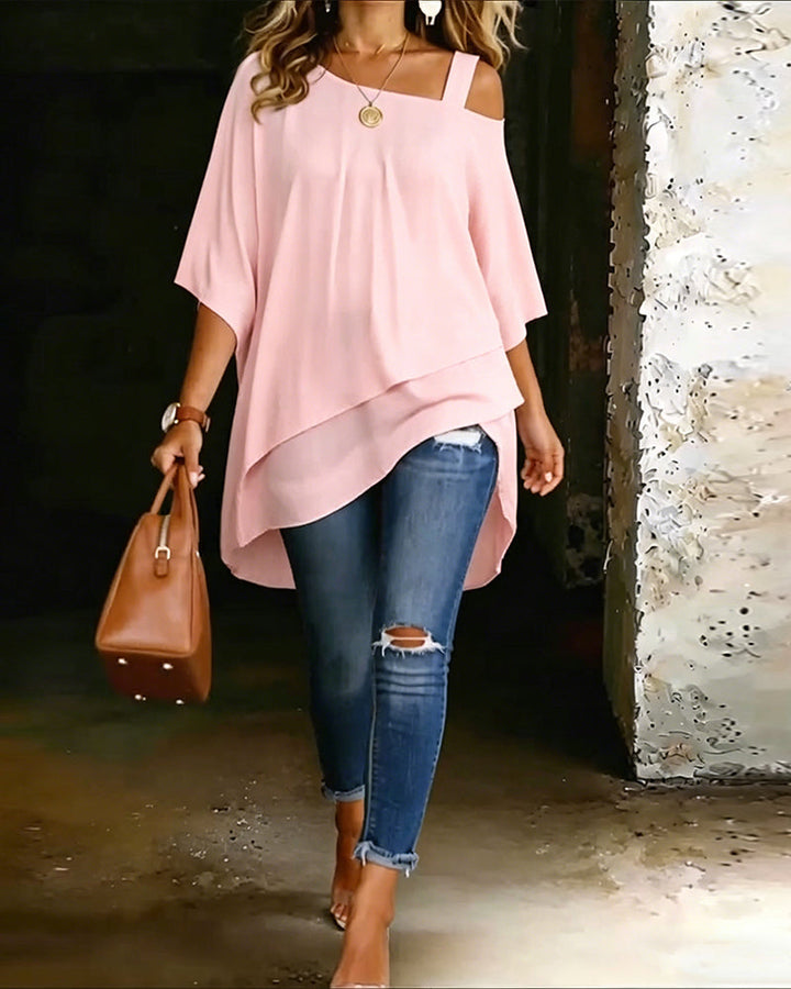 Light pink asymmetrical blouse with off-shoulder straps paired with ripped jeans and brown handbag in rustic setting.