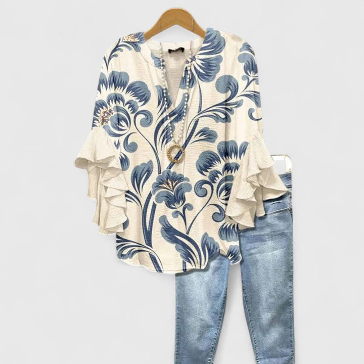 Ivory blouse with blue floral print and ruffled sleeves, paired with light jeans, hanging on wooden hanger.