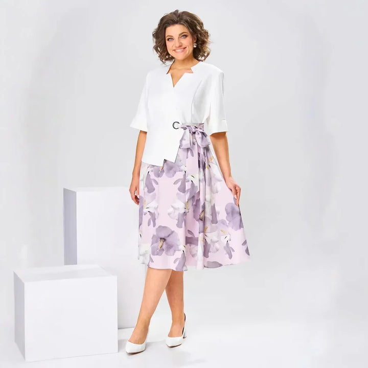 Woman in a white top and pastel floral midi skirt, posing in a white studio with geometric blocks.