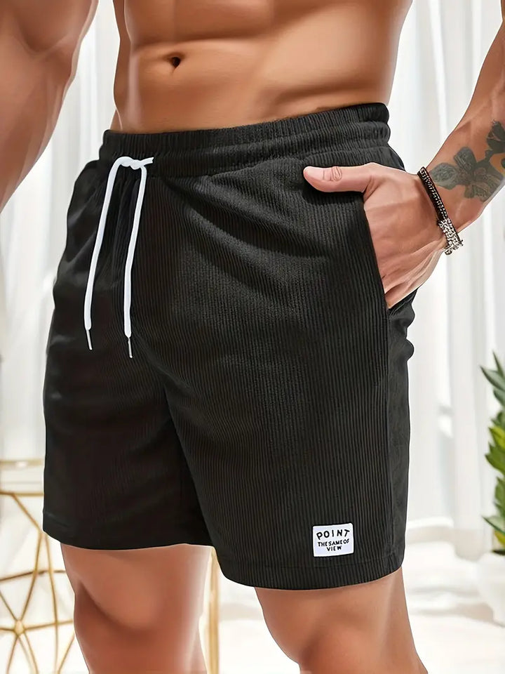 Close-up of black swimming trunks with drawstring, worn by model in stylish indoor setting.