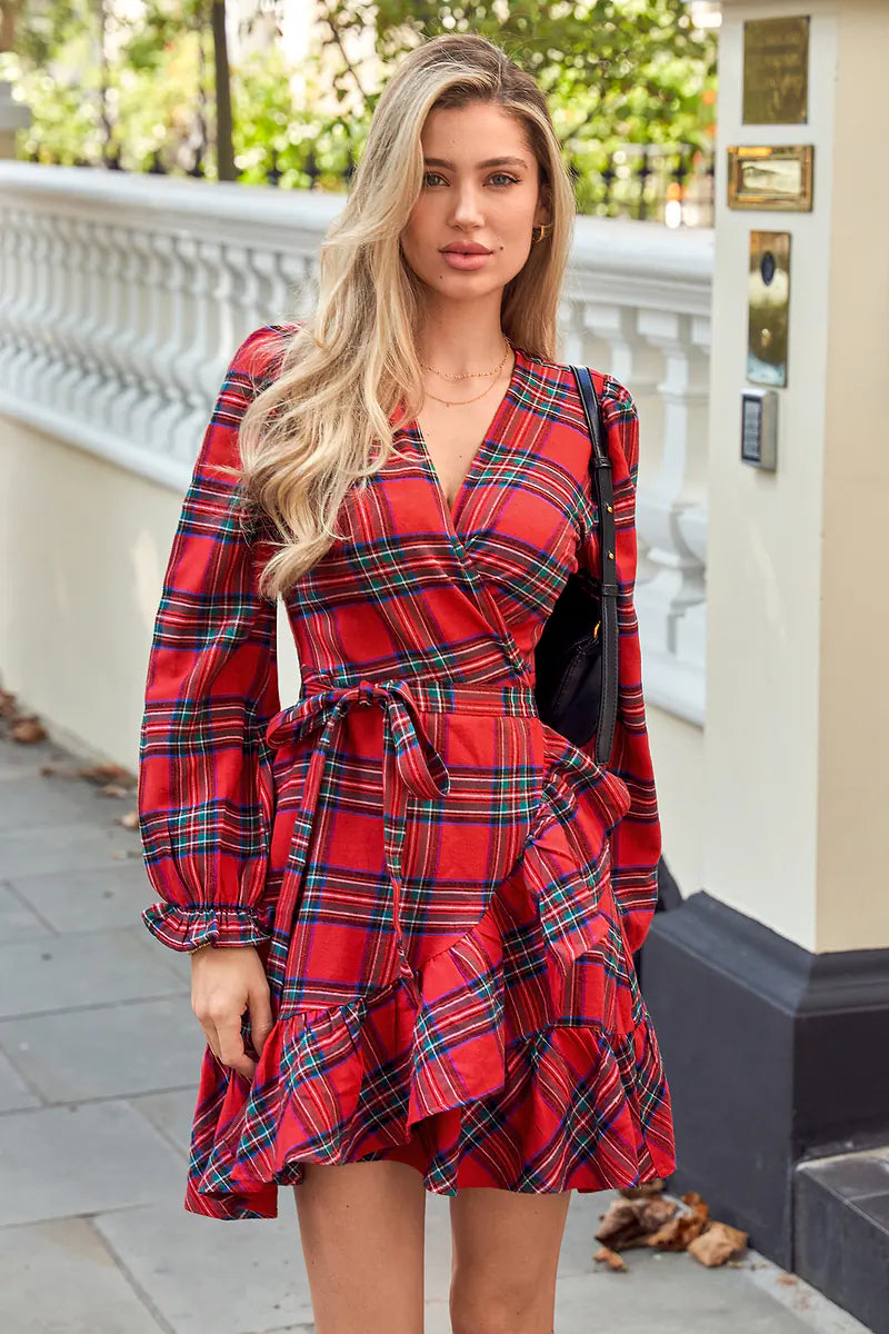 Woman in red plaid wrap dress with ruffle accents, standing near a white balustrade with lush greenery.