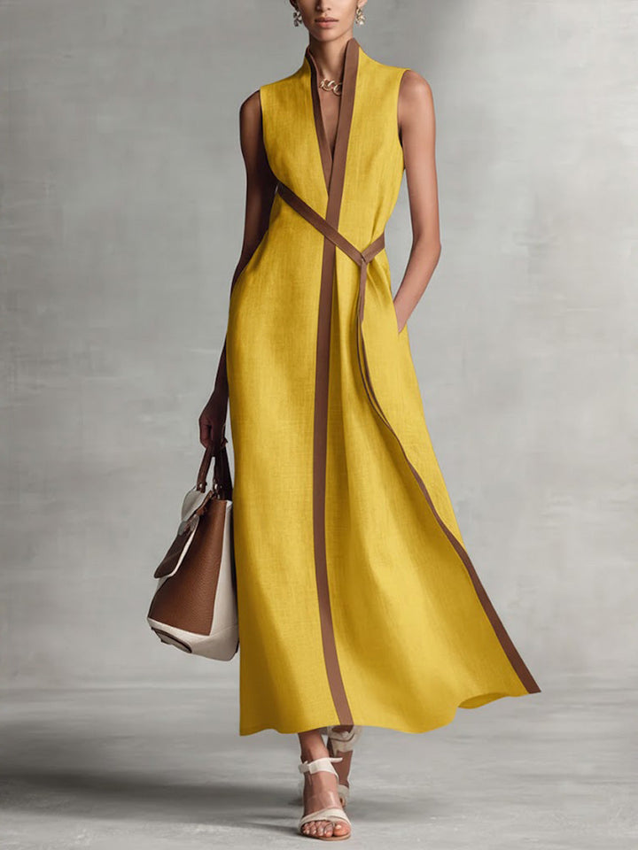 Vibrant sleeveless yellow maxi dress with brown trim, styled with a handbag and sandals in a studio setting.