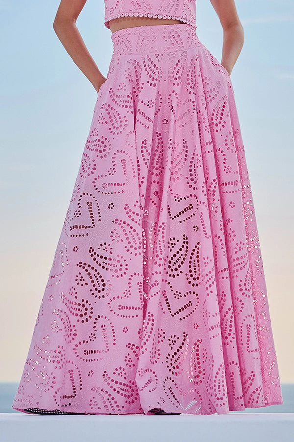 Model in a pink embroidered high-waist maxi skirt with hands in pockets against a clear sky.