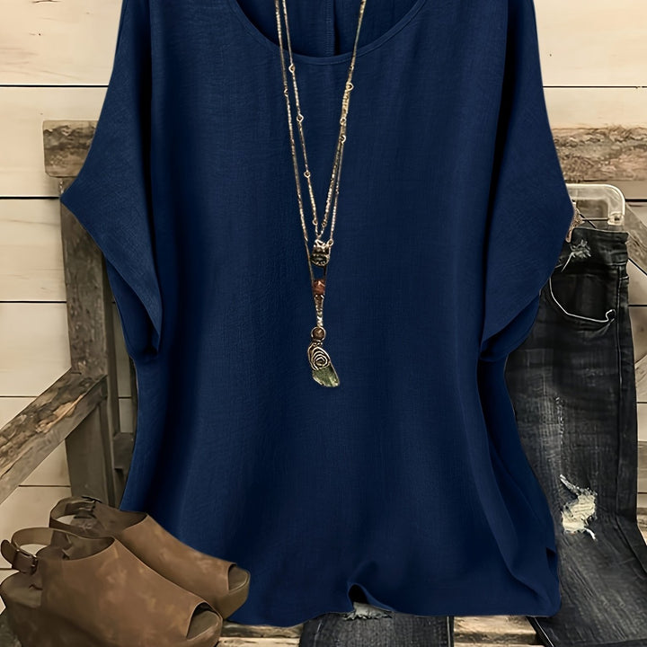 Deep blue loose summer top on hanger with necklace, sandals, and jeans on rustic bench.