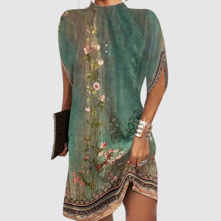 Patterned green and beige knee-length dress with floral design, loose fit, paired with gold bangles and clutch against gray.