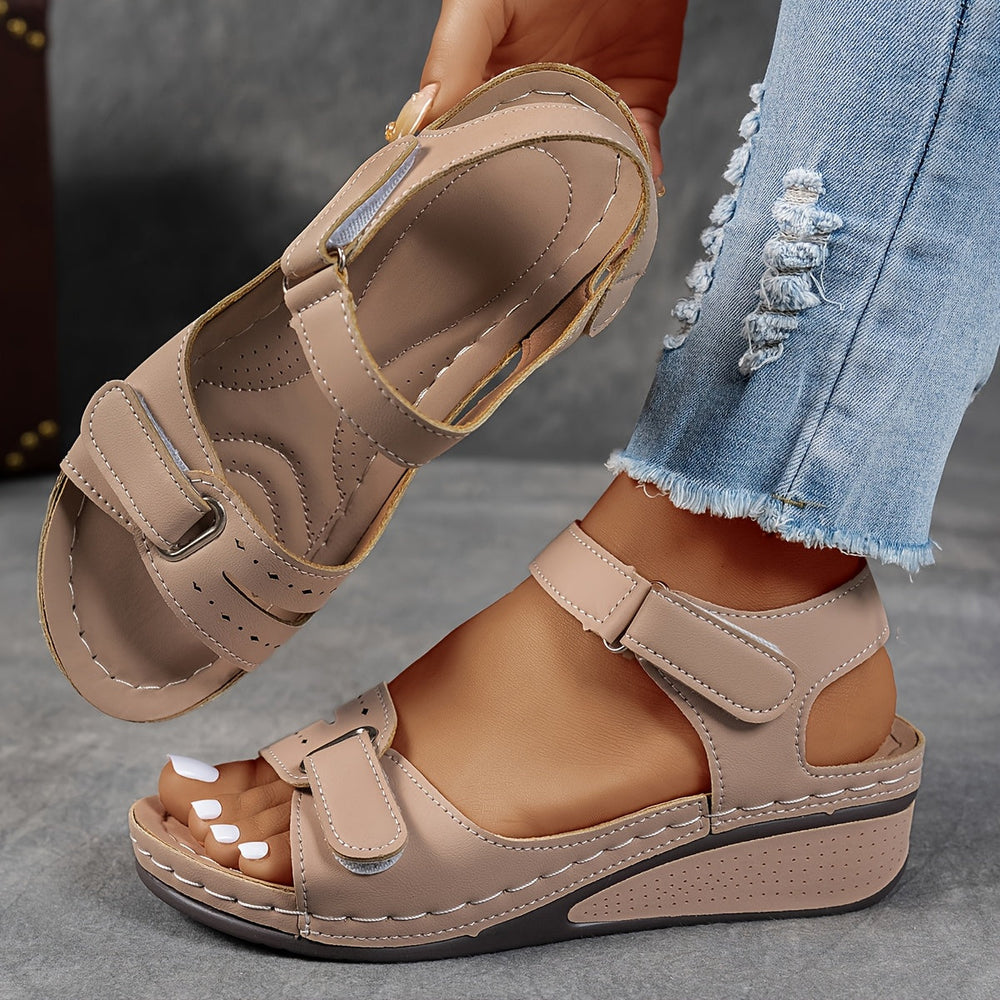 Beige orthopedic sandal with adjustable straps and padded footbed, worn with distressed jeans on a gray background.