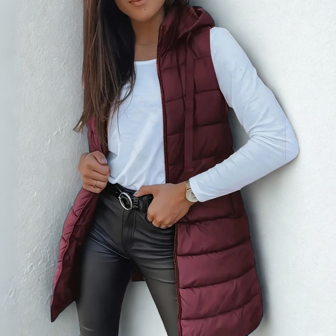 Burgundy sleeveless puffer vest with hood over white top and black pants, white textured background.