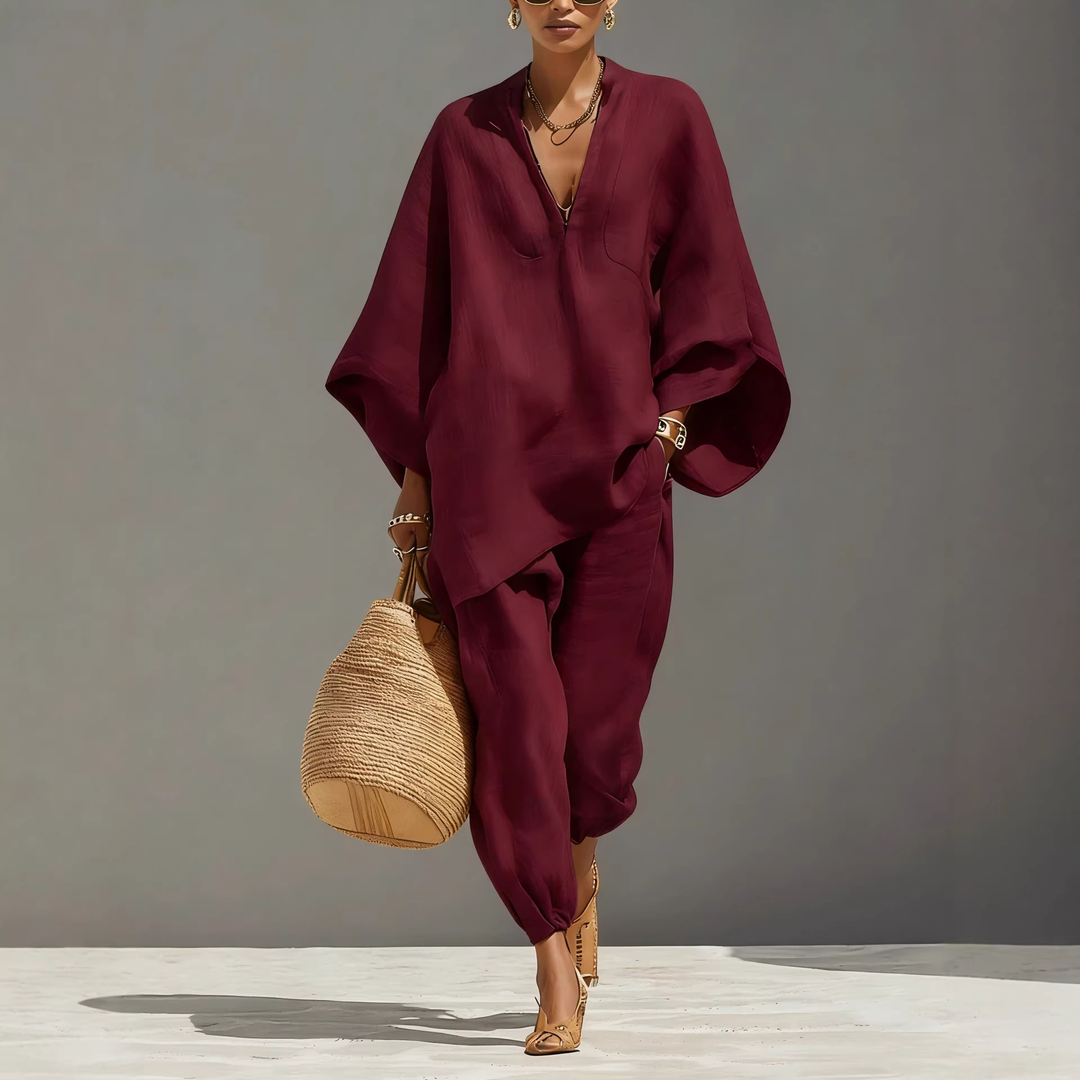 Model in burgundy batwing sleeve V-neck lounge set holding woven bag, studio background.