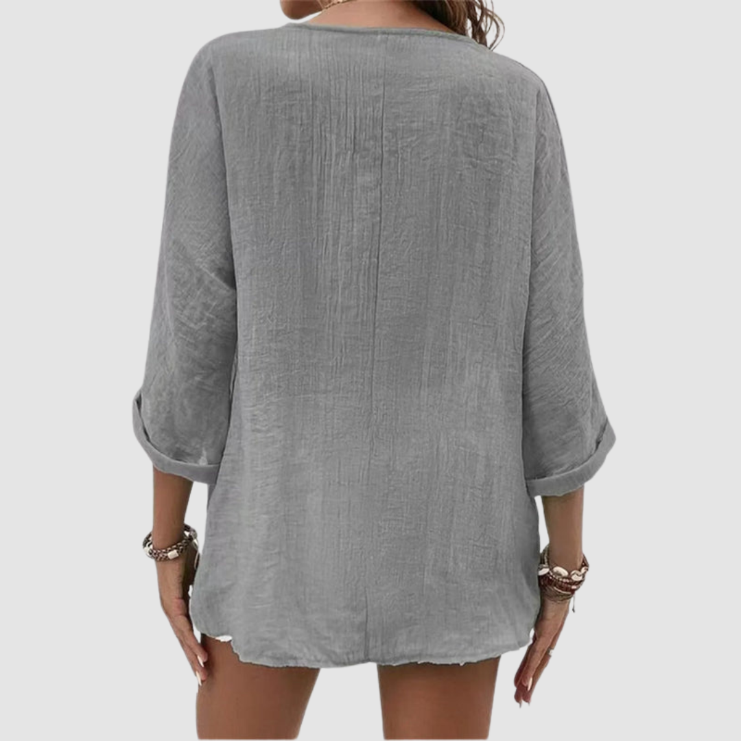 Back view of woman wearing a grey three-quarter sleeve blouse, accessorized with bracelets, against a plain background.