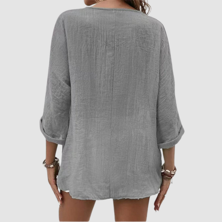 Back view of woman wearing a grey three-quarter sleeve blouse, accessorized with bracelets, against a plain background.