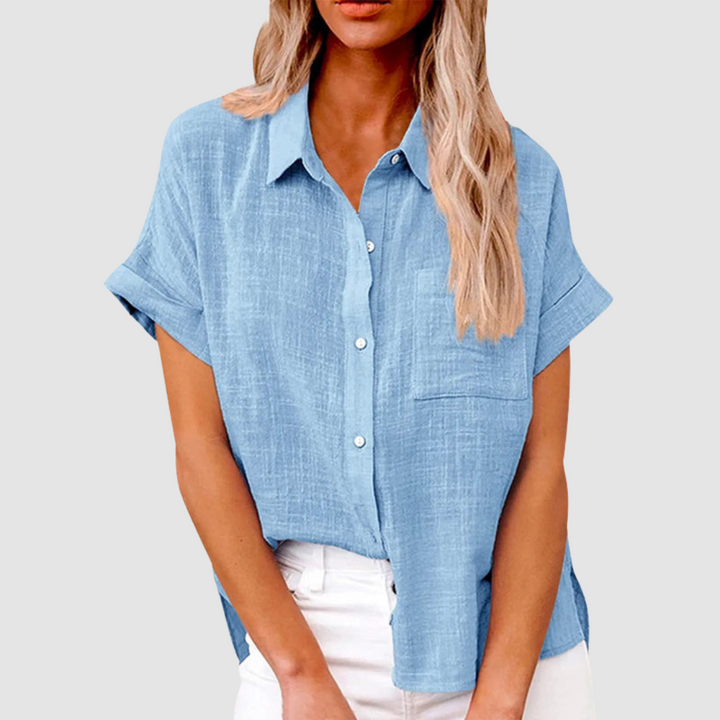 Blue casual blouse with short sleeves and front buttons, worn in white jeans. Studio background.