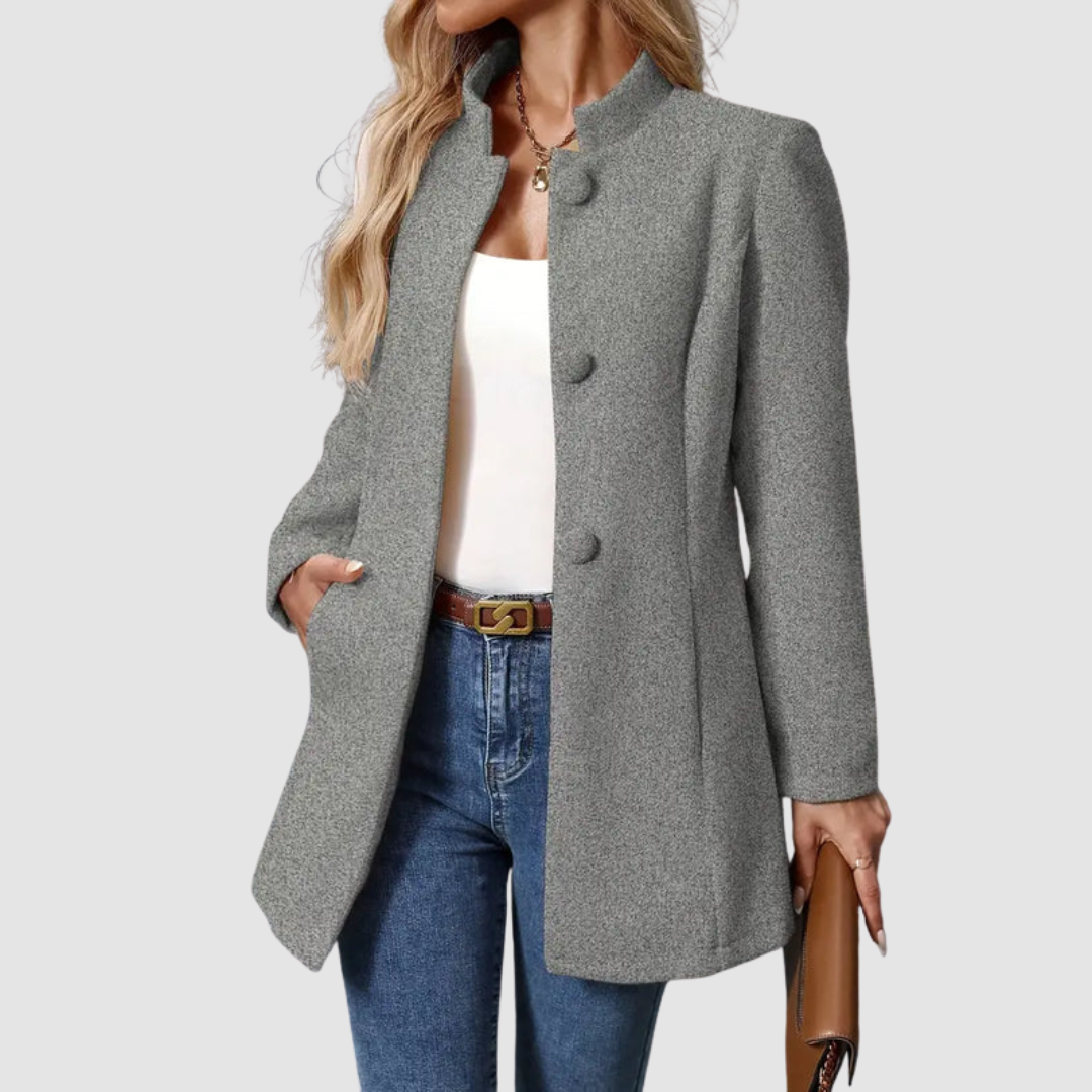 Gray jacket, large buttons, white top underneath, jeans, holding clutch, plain background.