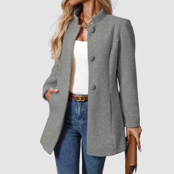 Gray jacket, large buttons, white top underneath, jeans, holding clutch, plain background.