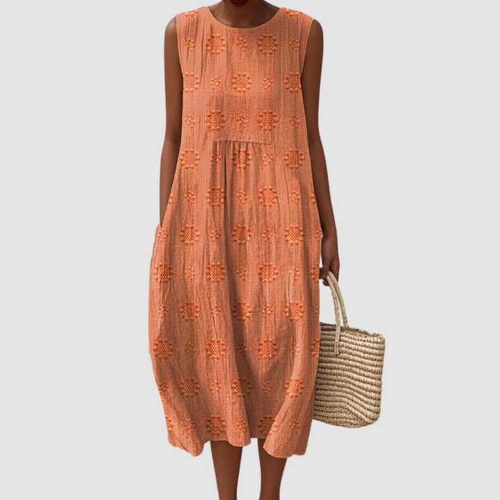 Orange sleeveless summer dress with floral patterns, model holding a woven basket, white background.
