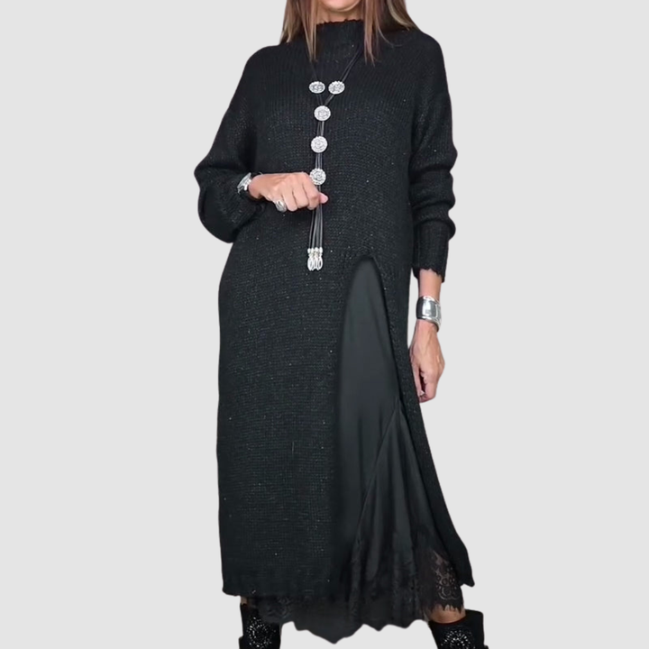 Black dress with layered fabric and long pendant necklace, woman posing against gray background.